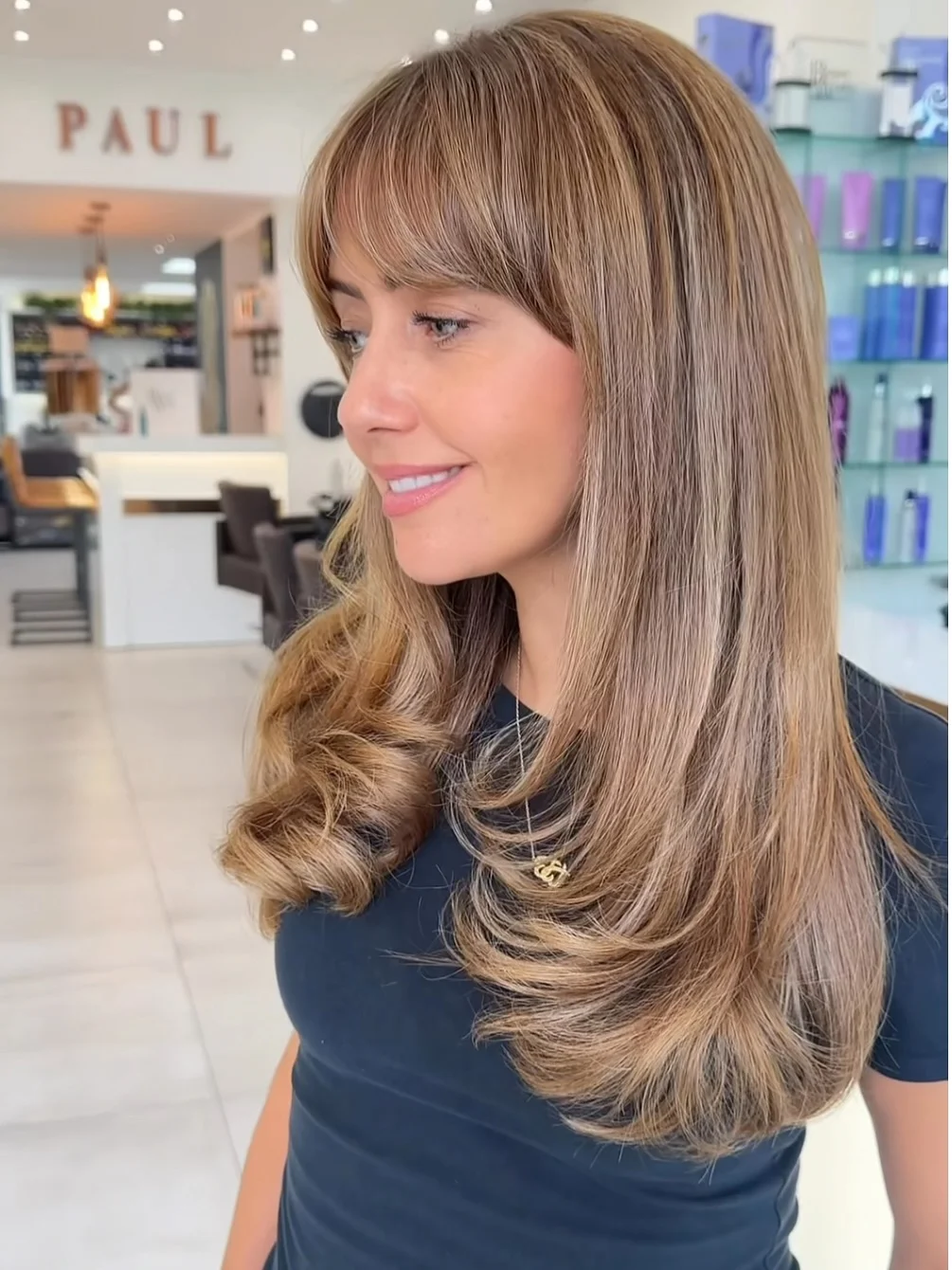 toffee summer hair color for tan skin 2026 Feathered Toffee Blowout With Curtain Bangs